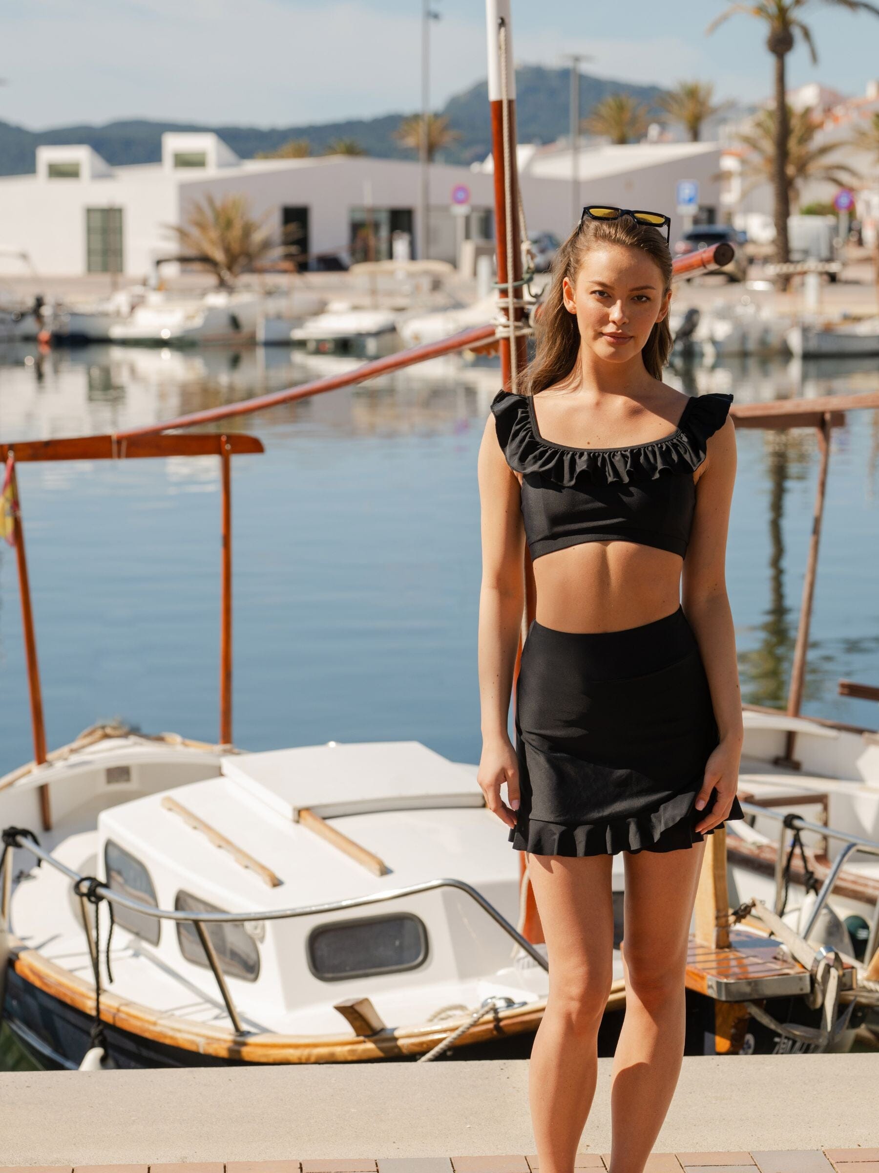 Woman in a black ruffle top and ruffle skirt standing by a marina 