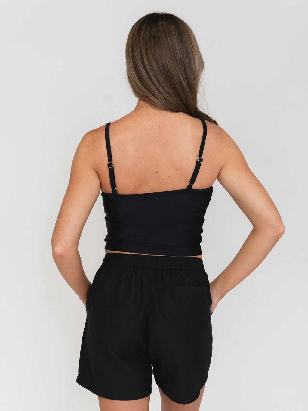 Woman wearing a black tankini and black boardshorts set on a white background