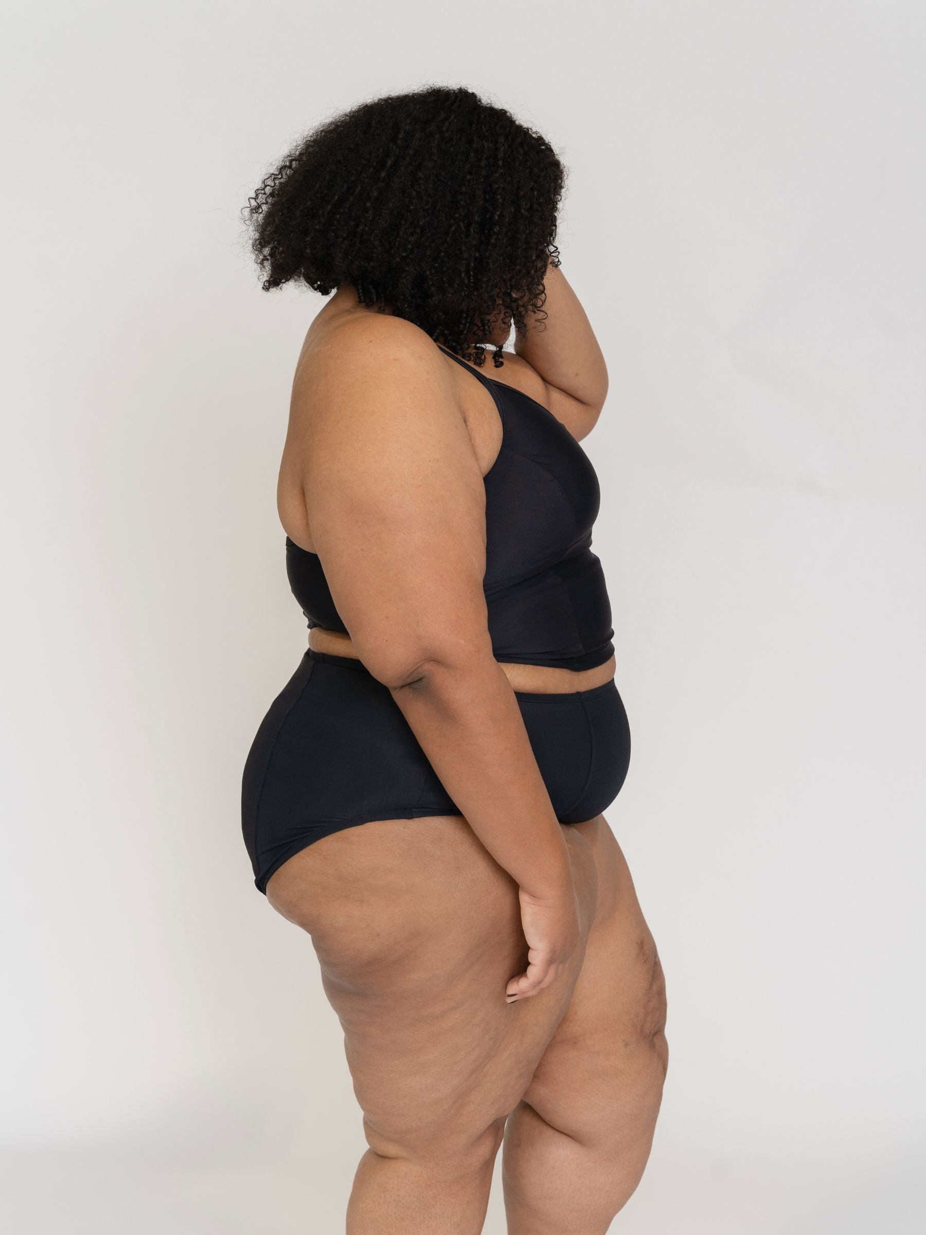 Woman wearing a black tankini set against a white background from the side