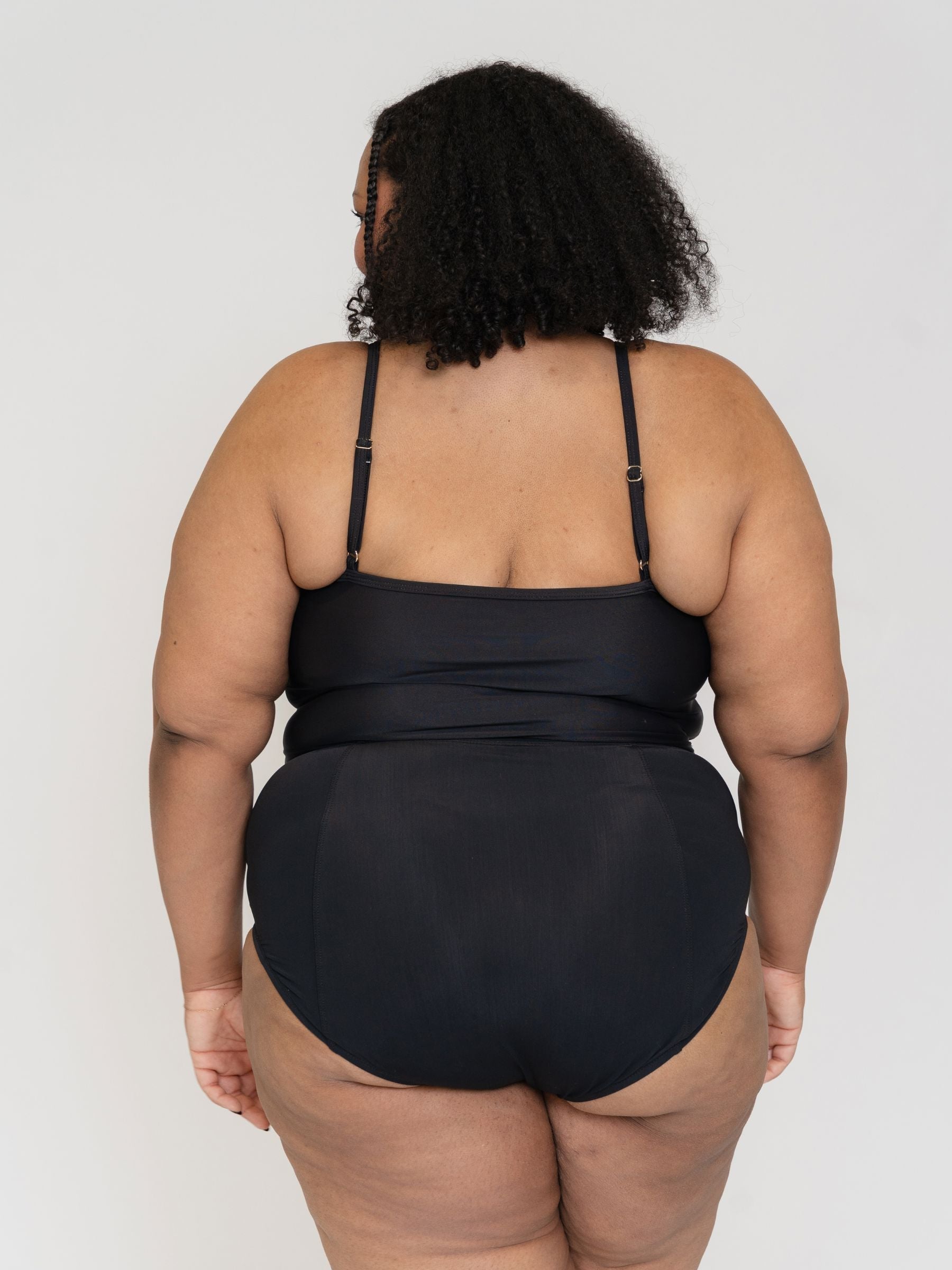 woman wearing a black tankini set against a white background back view