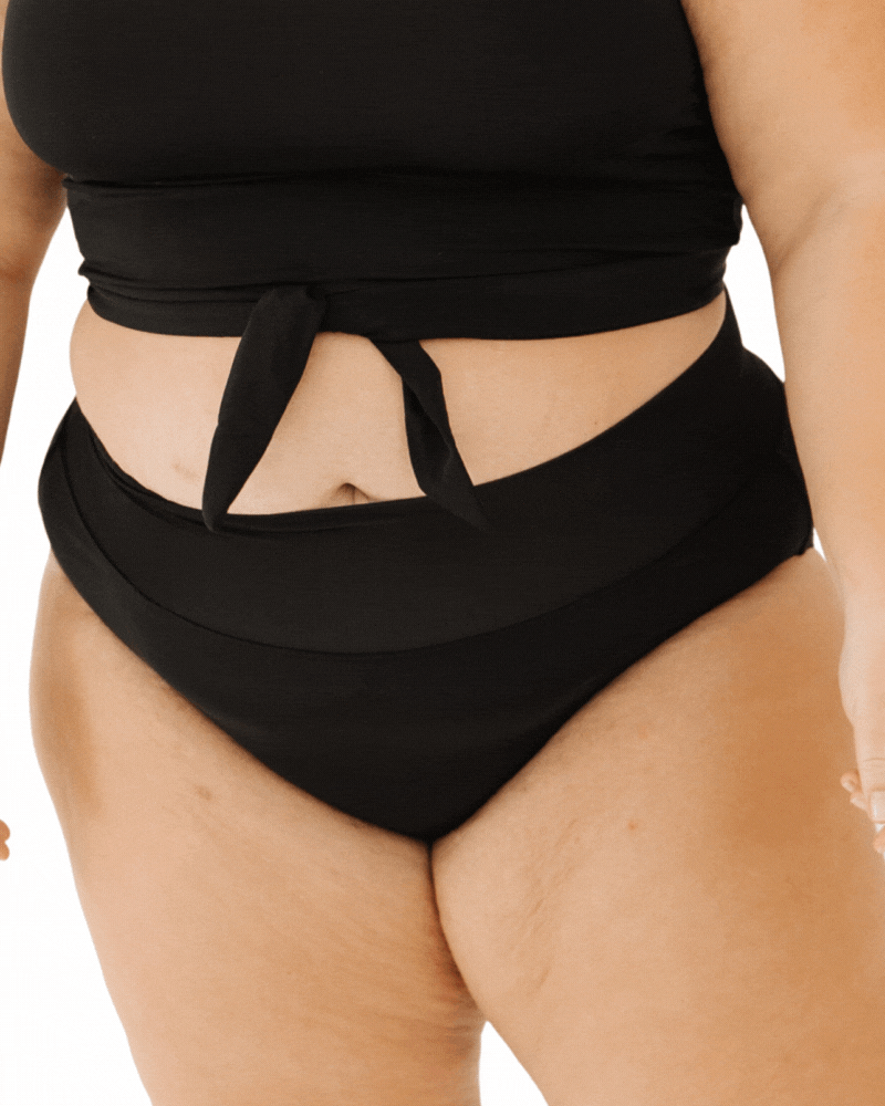 Close up GIF of a woman in black classic swim bottoms and a black knotted crop on a white background  