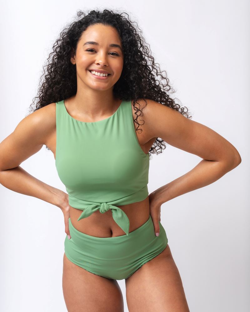 Photo of a woman wearing a light green knotted swim crop top and a dark green floral/ light green reversible swim bottom- light green side