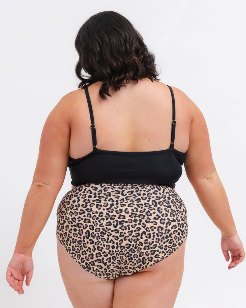woman wearing a black sports bra and a leopard bikini bottom on a white background from behind 