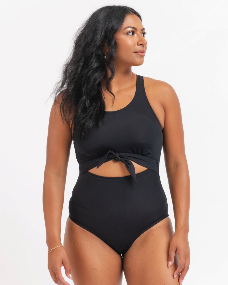 A model wearing a black one-piece swimsuit with a knotted front detail.