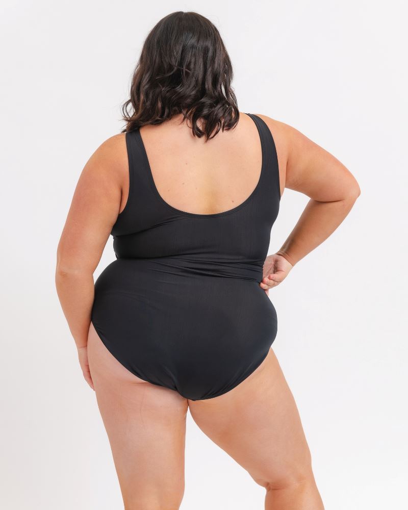 back view of a woman wearing a black knotted one piece suit with a white background