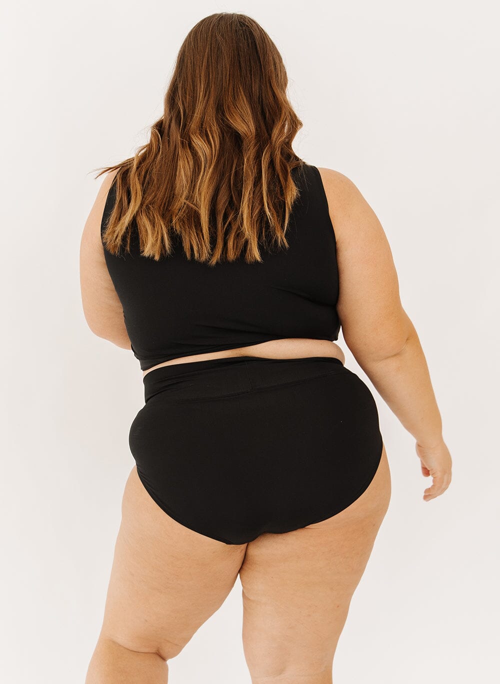 Photo of a woman in black classic swim bottoms and black swim crop top back angle on a white background 