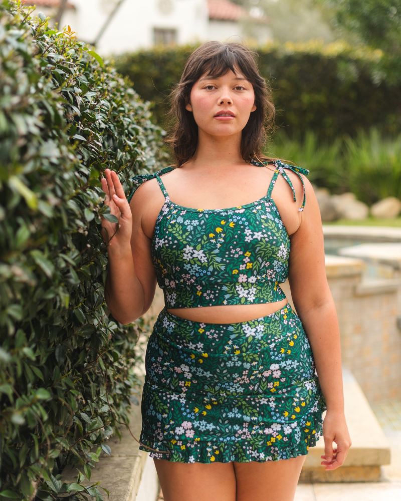 Photo of a woman wearing a dark green floral shoulder-tie swim crop top and a dark green floral swim skirt
