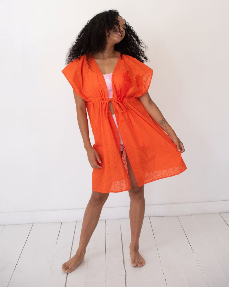 Photo of a woman wearing an orange Kaftan cover up and a pink checkered swim bralette and pink checkered swim short