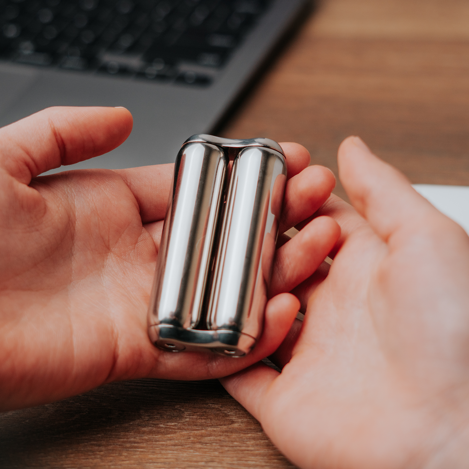 eam_Junior | Person holding stainless steel ONO Roller fidget toy on wooden desk