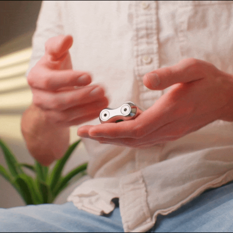 eam_Mini | Hands holding silver ONO Roller Steel fidget toy with white eyes detail, lifestyle shot