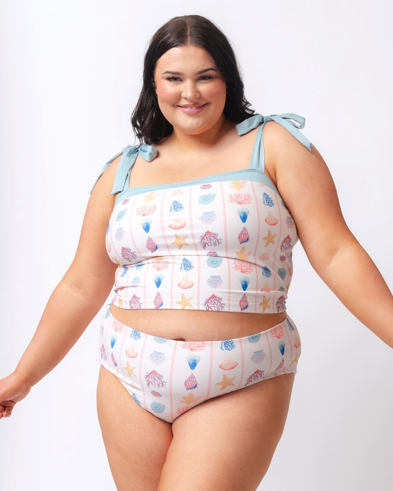 Photo of a woman wearing a seashell striped high waist swim bottom and a seashell striped shoulder-tie swim crop